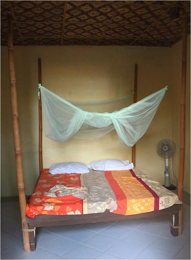 Marios Scuba Diving and Homestay. Pokoj s nezbytnou moskytiérou. Kromě postele tu ještě najdete jednoduchou malou poličku a stolek z bambusu.